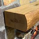 A live edge style fireplace mantel, made from ash wood, mounted on a stone wall.