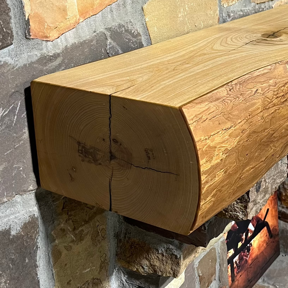 A live edge style fireplace mantel, made from ash wood, mounted on a stone wall.