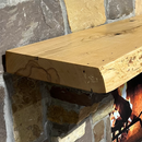 A live edge style fireplace mantel, made from ash wood, mounted on a stone wall.