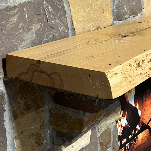 A live edge style fireplace mantel, made from ash wood, mounted on a stone wall.