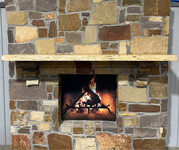 A live edge style fireplace mantel, made from ash wood, mounted on a stone wall.