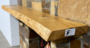 A live edge style fireplace mantel, made from ash wood, mounted on a stone wall.