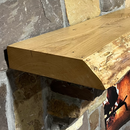 A live edge style fireplace mantel, made from ash wood, mounted on a stone wall.