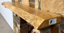 A live edge style fireplace mantel, made from ash wood, mounted on a stone wall.