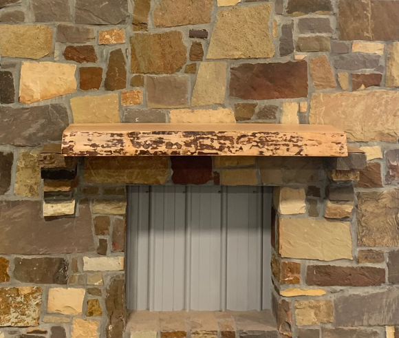 A live edge style fireplace mantel, made from birch wood, mounted on a stone wall.