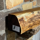 A live edge style fireplace mantel, made from bois d'arc wood, mounted on a stone wall.
