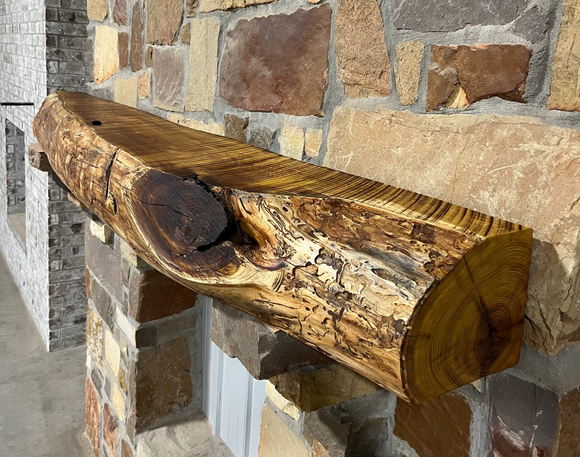 A live edge style fireplace mantel, made from bois d'arc wood, mounted on a stone wall.