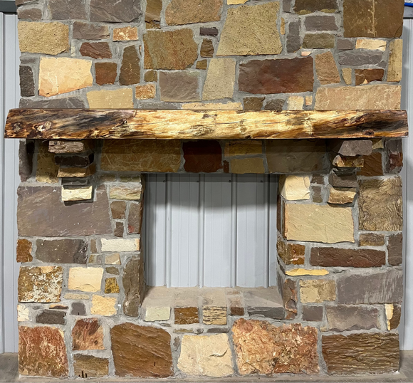 A live edge style fireplace mantel, made from bois d'arc wood, mounted on a stone wall.