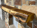 A live edge style fireplace mantel, made from bois d'arc wood, mounted on a stone wall.