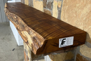 A live edge style fireplace mantel, made from bois d'arc wood, mounted on a stone wall.