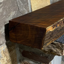 A live edge style fireplace mantel, made from bois d'arc wood, mounted on a stone wall.