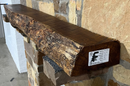 A live edge style fireplace mantel, made from bois d'arc wood, mounted on a stone wall.