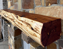 A live edge style fireplace mantel, made from cedar wood, mounted on a stone wall.