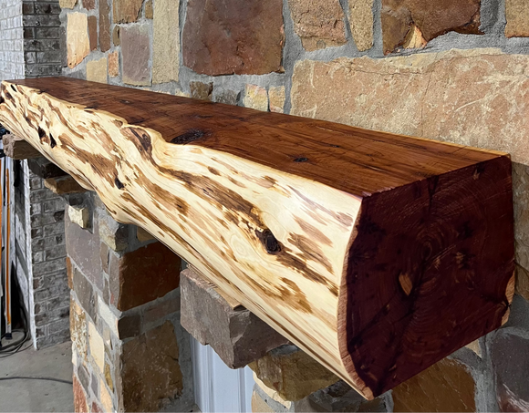 A live edge style fireplace mantel, made from cedar wood, mounted on a stone wall.