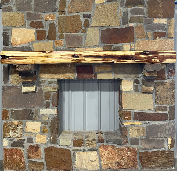 A live edge style fireplace mantel, made from cedar wood, mounted on a stone wall.