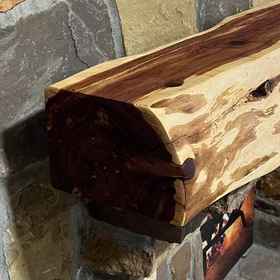 A live edge style fireplace mantel, made from cedar wood, mounted on a stone wall.
