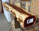A live edge style fireplace mantel, made from cedar wood, mounted on a stone wall.
