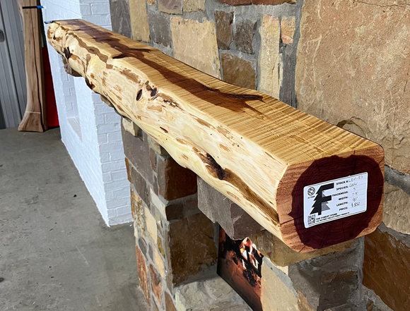 A live edge style fireplace mantel, made from cedar wood, mounted on a stone wall.
