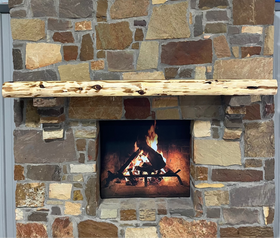 A live edge style fireplace mantel, made from cedar wood, mounted on a stone wall.
