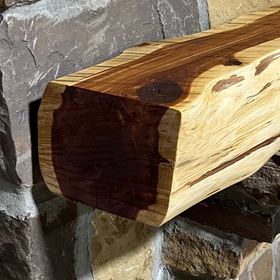 A live edge style fireplace mantel, made from cedar wood, mounted on a stone wall.
