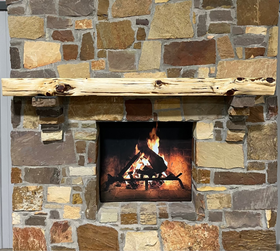 A live edge style fireplace mantel, made from cedar wood, mounted on a stone wall.
