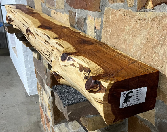 A live edge style fireplace mantel, made from cedar wood, mounted on a stone wall.
