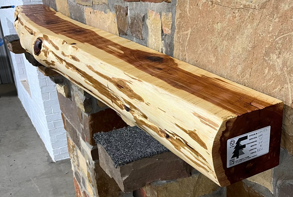 A live edge style fireplace mantel, made from cedar wood, mounted on a stone wall.
