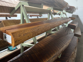 A live edge style fireplace mantel, made from cherry wood, displayed on a rack.