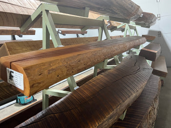 A live edge style fireplace mantel, made from cherry wood, displayed on a rack.