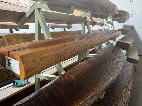 A live edge style fireplace mantel, made from cherry wood, displayed on a rack.