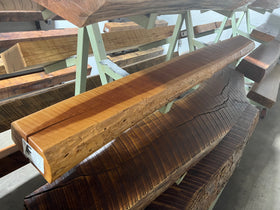 A live edge style fireplace mantel, made from cherry wood, displayed on a rack.