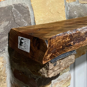 A live edge style fireplace mantel, made from cherry wood, mounted on a stone wall.