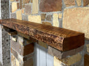 A live edge style fireplace mantel, made from cherry wood, mounted on a stone wall.