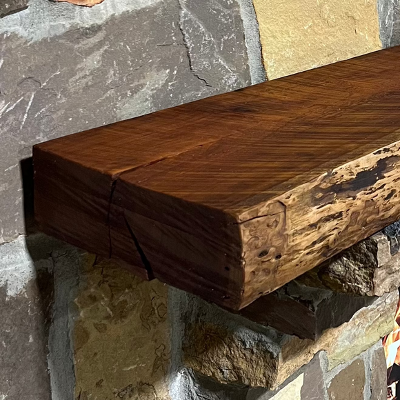 A live edge style fireplace mantel, made from cherry wood, mounted on a stone wall.