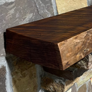 A live edge style fireplace mantel, made from cherry wood, mounted on a stone wall.