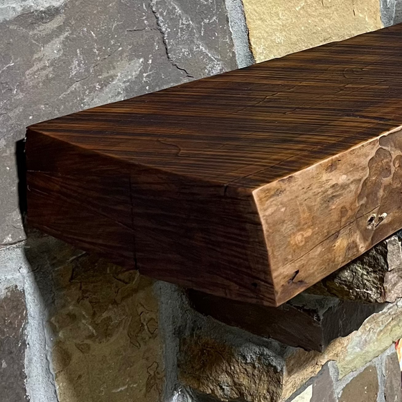 A live edge style fireplace mantel, made from cherry wood, mounted on a stone wall.