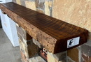 A live edge style fireplace mantel, made from cherry wood, mounted on a stone wall.