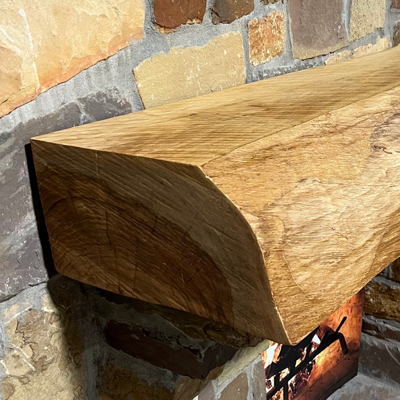 A live edge style fireplace mantel, made from pecan wood, mounted on a stone wall.
