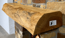 A live edge style fireplace mantel, made from pecan wood, mounted on a stone wall.
