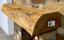 A live edge style fireplace mantel, made from pine wood, mounted on a stone wall.
