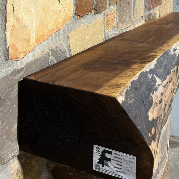 A live edge style fireplace mantel, made from walnut wood, mounted to a rock wall.
