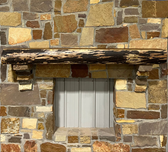 A live edge style fireplace mantel, made from walnut wood, mounted to a rock wall.
