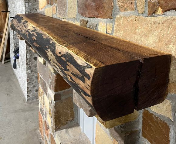 A live edge style fireplace mantel, made from walnut wood, mounted to a rock wall.