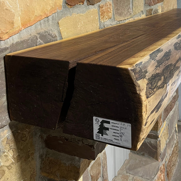 A live edge style fireplace mantel, made from walnut wood, mounted to a rock wall.