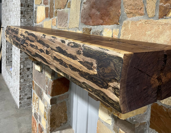 A live edge style fireplace mantel, made from walnut wood, mounted to a rock wall.