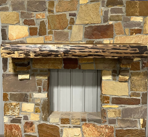 A live edge style fireplace mantel, made from walnut wood, mounted to a rock wall.