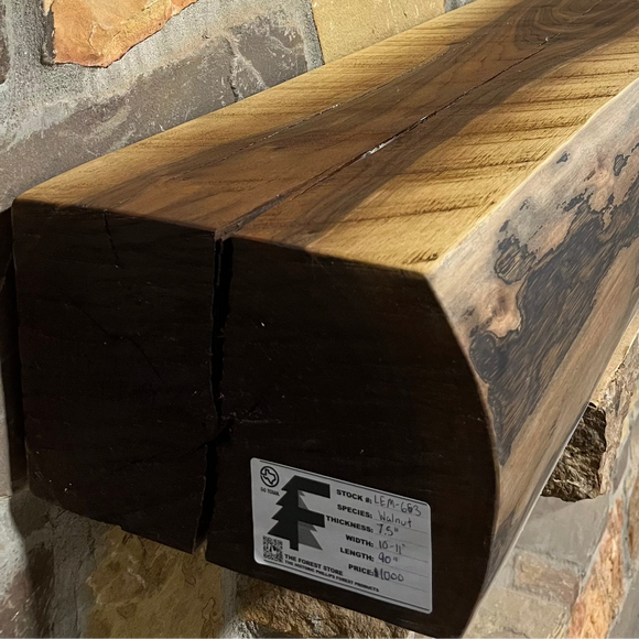 A live edge style fireplace mantel, made from walnut wood, mounted to a rock wall.