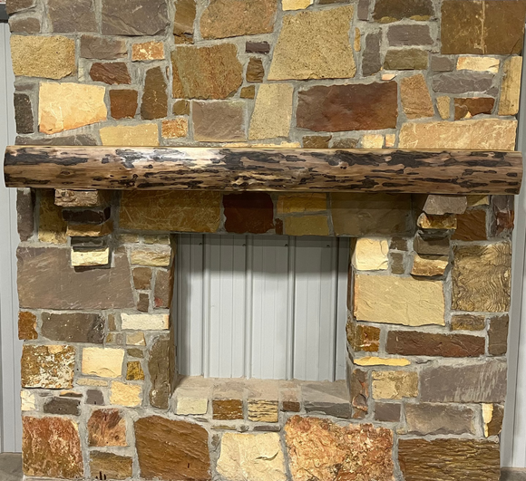 A live edge style fireplace mantel, made from walnut wood, mounted to a rock wall.