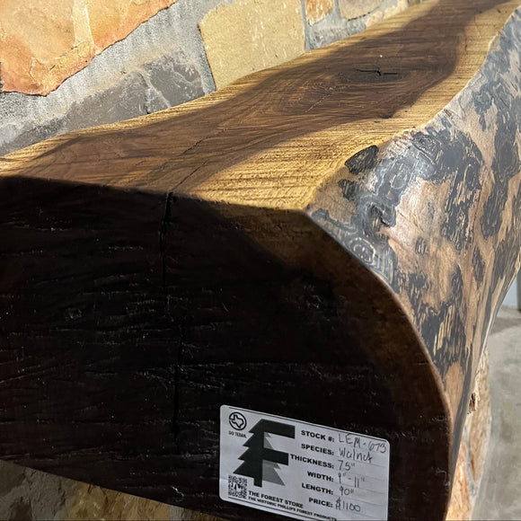 A live edge style fireplace mantel, made from walnut wood, mounted to a rock wall.