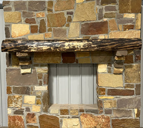 A live edge style fireplace mantel, made from walnut wood, mounted to a rock wall.
